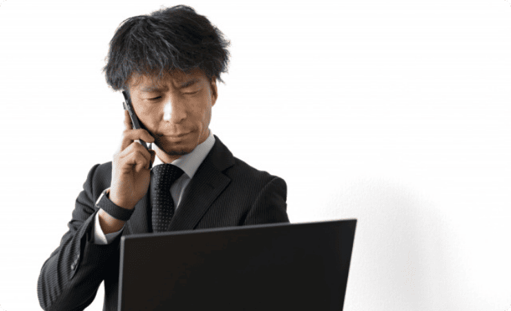 スマホで通話しながらノートパソコンを眺める男性