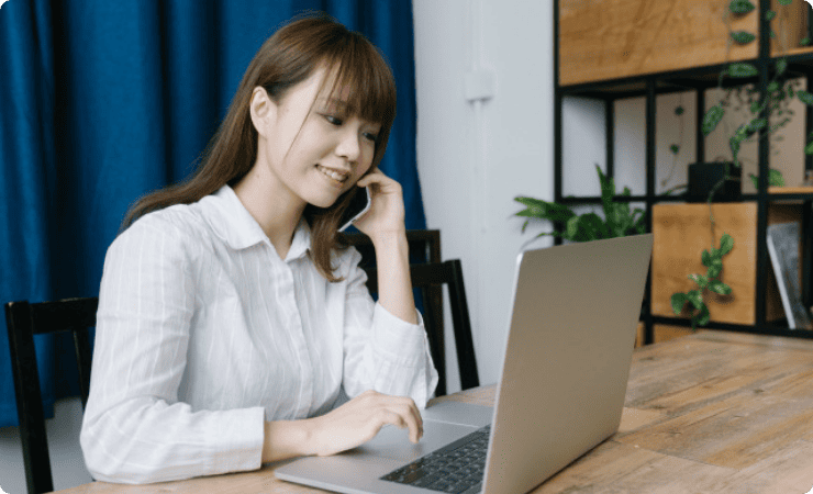 ノートパソコンを操作しながらスマホで通話する女性